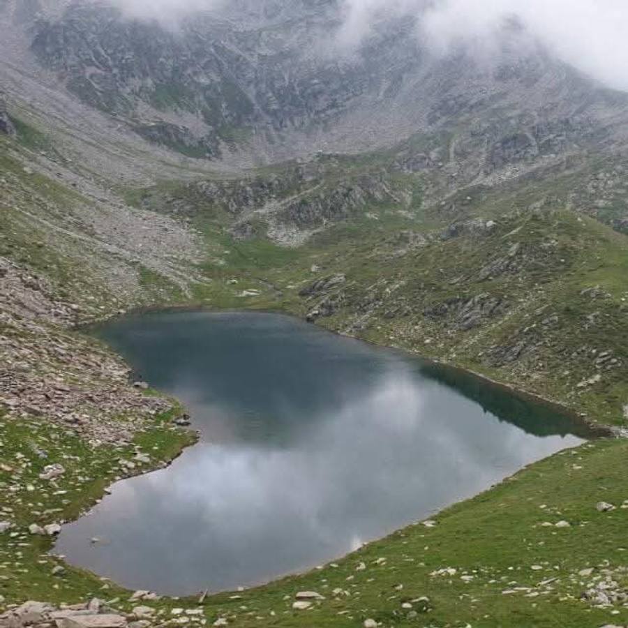 A still tarn on the plateau reflecting low cloud, ringed by grass and scree below grey crags.