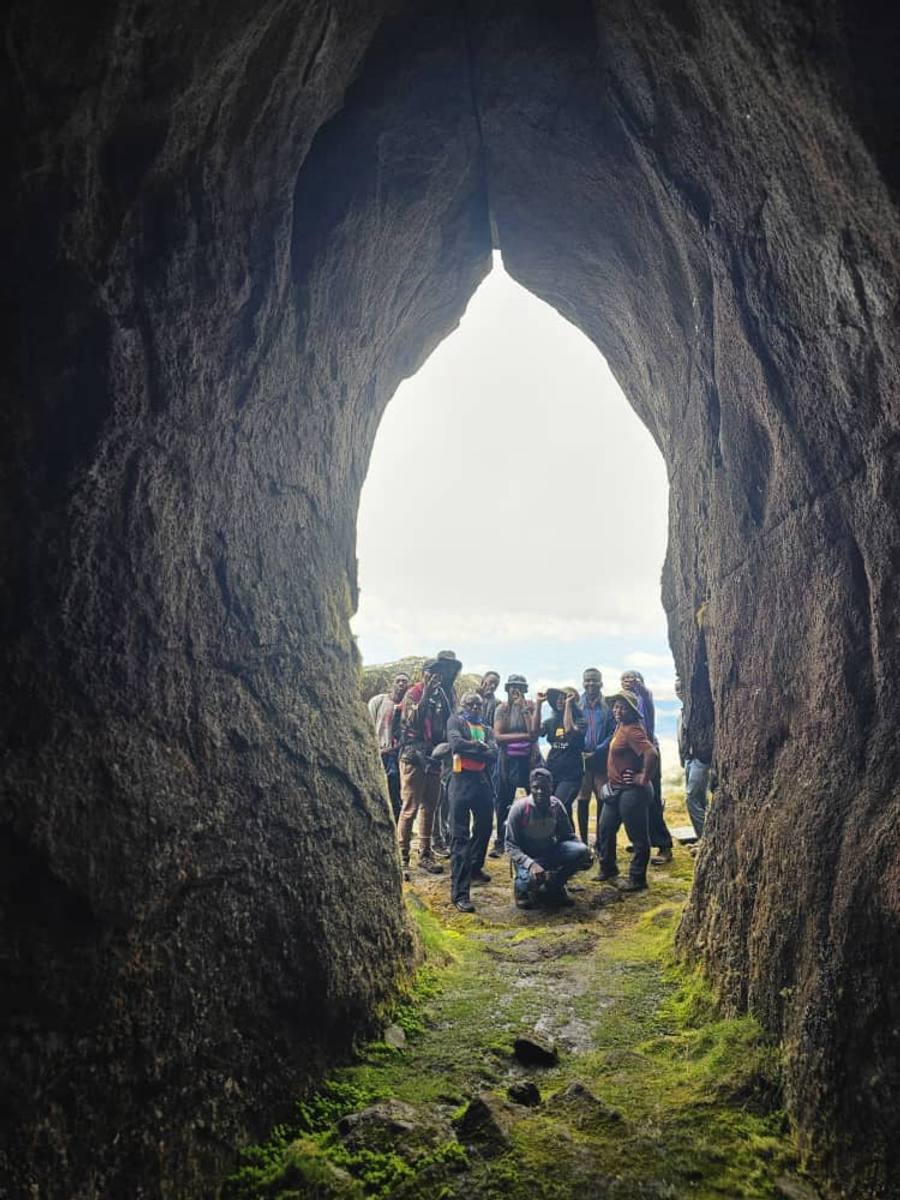 A group of walkers framed in the tall arched mouth of a cave near Sapitwa Peak, looking back towards the light.