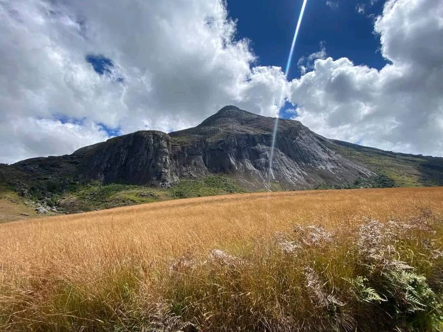 Chambe peak rising above a wide field of golden plateau grass under towering white cloud.