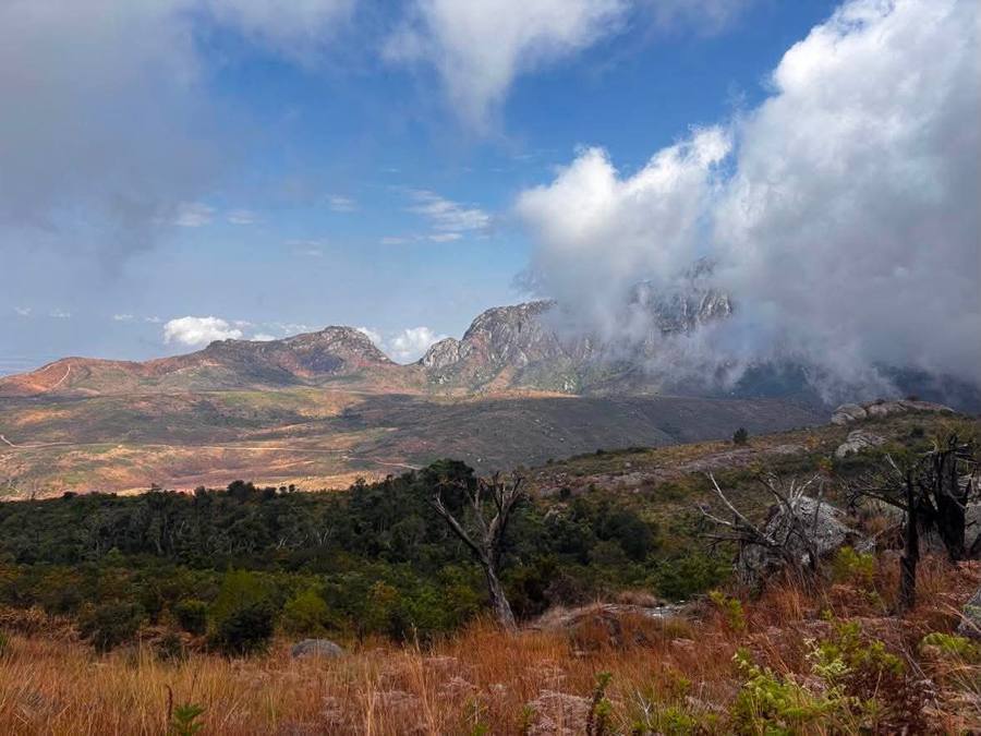 Cloud pours over the massif ridge above burnt grassland and bare trees.