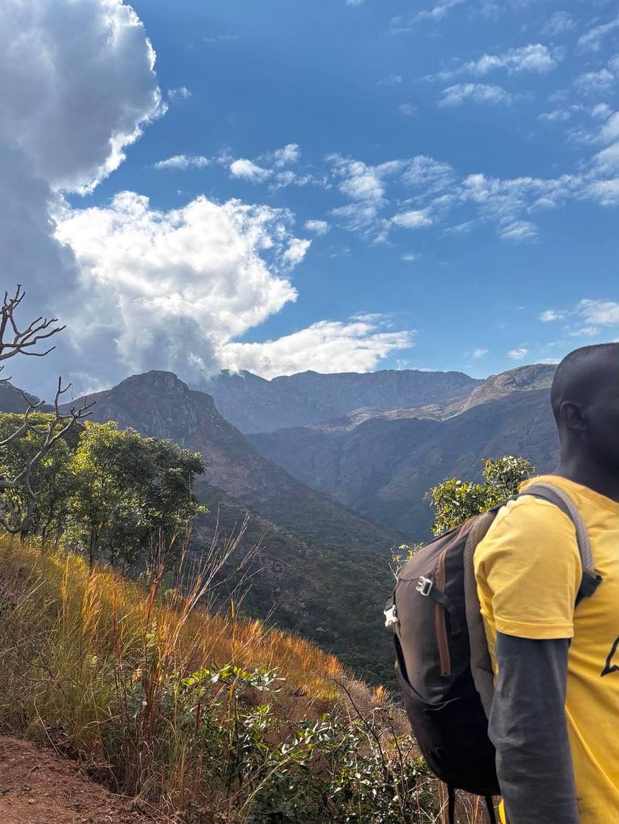 A guide pauses on a hillside path and looks out across the ridges of the Mulanje massif.