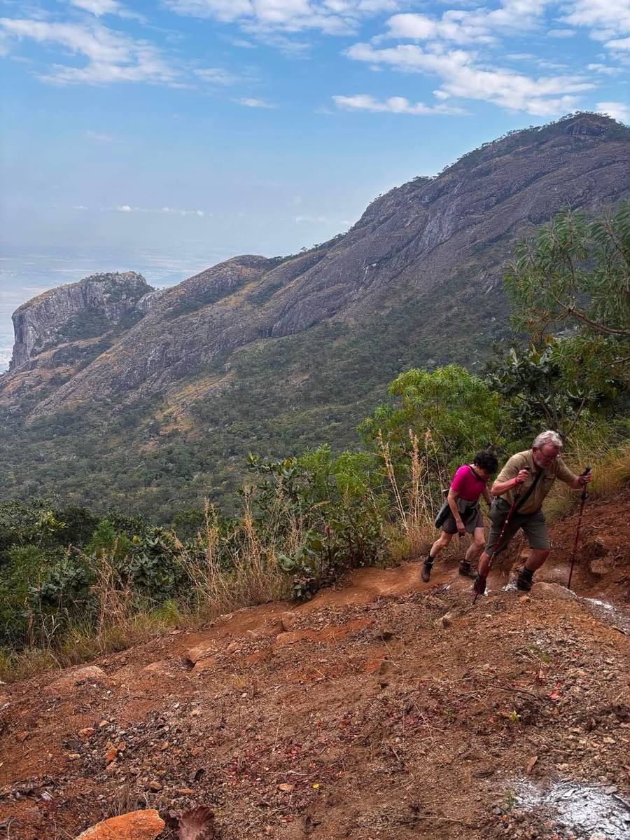 Two hikers with trekking poles climb a steep eroded trail high on the mountain.