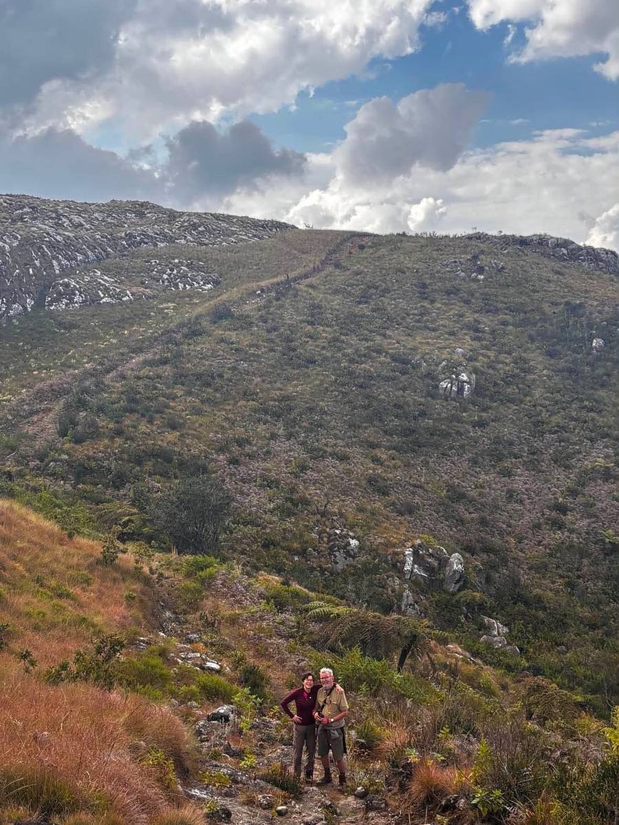 Two hikers stand on an open slope, dwarfed by the plateau and its footpath behind them.