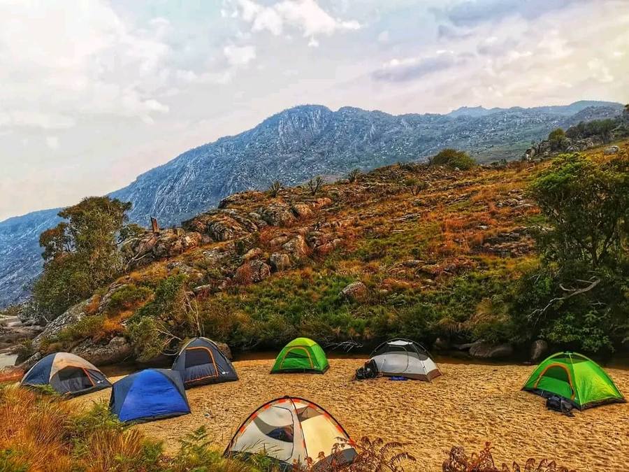 Tents pitched on sand beside Malosa pool on the Mulanje plateau, with the massif behind in evening light.