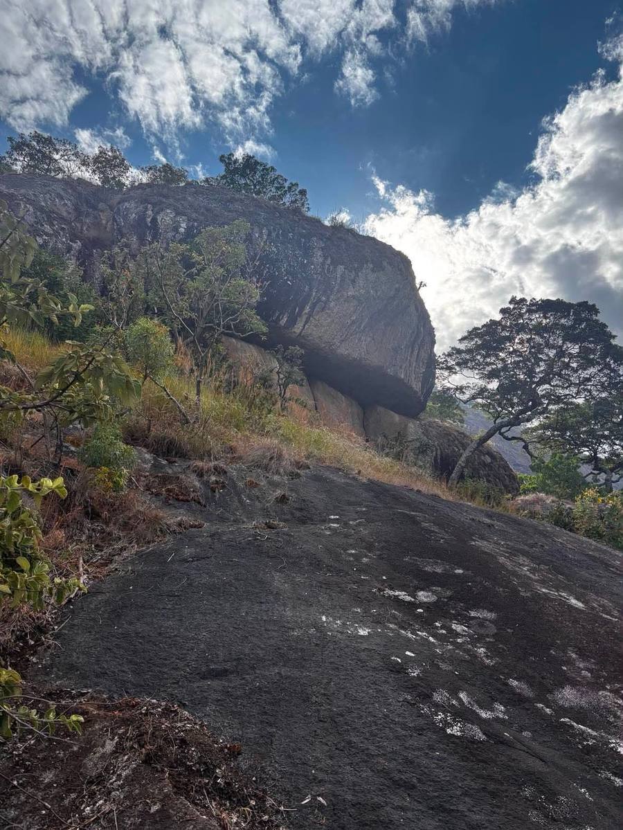 A large overhanging boulder juts from a ridge above a smooth granite slab.