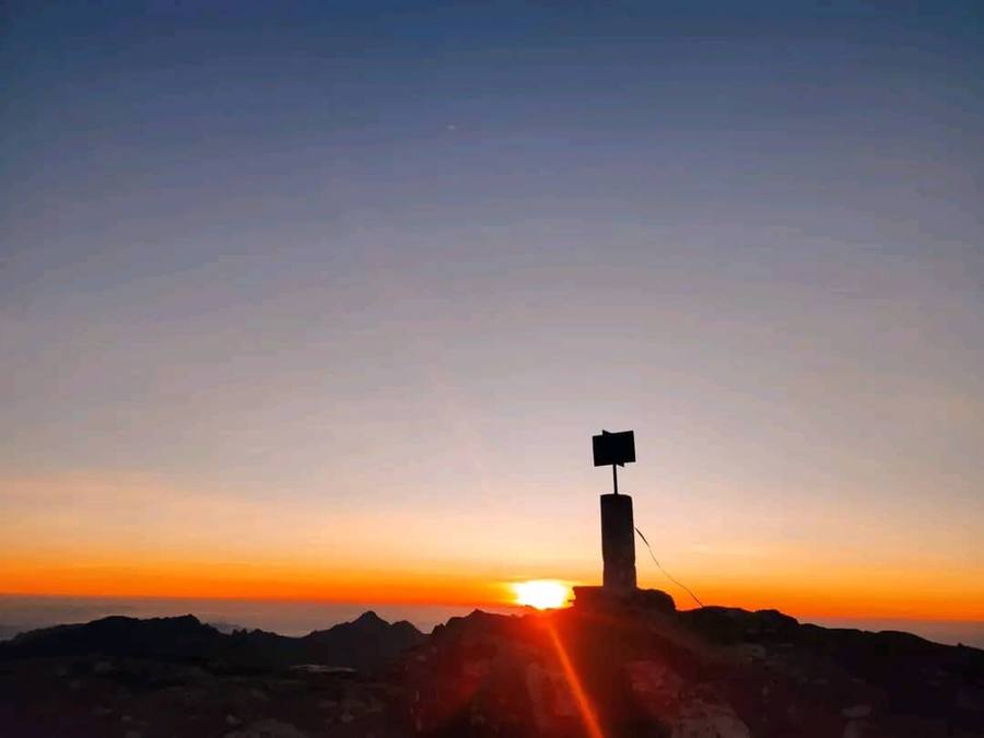 Sunrise seen from the top of Sapitwa Peak, the summit marker silhouetted against an orange horizon above the cloud.