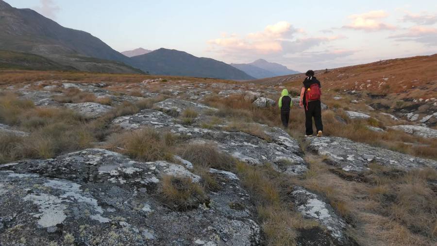 Two walkers cross lichen-covered slabs on the plateau in the last light.