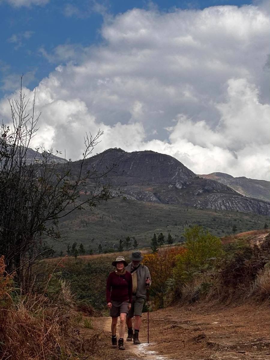 Two walkers come down a dirt track with a granite ridge rising behind them.